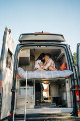 Niedriger Winkel Seitenansicht der reisenden Paar sitzt auf dem Bett im Wohnmobil und umarmt während der Sommerreise - ADSF37713