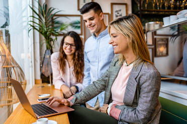 Side view of content female coach talking at table in cafeteria with employees with laptop - ADSF37752