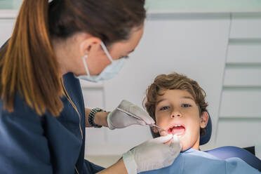 Von oben weiblicher Arzt und Krankenschwester mit zahnärztlichen Werkzeugen Überprüfung und Behandlung der Zähne des Jungen während der Arbeit in der zeitgenössischen Klinik - ADSF37771