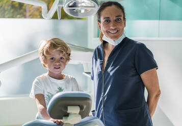 Frauen in medizinischer Uniform bereiten sich auf die Untersuchung eines kleinen Jungen vor, während sie in einer modernen Zahnklinik arbeiten - ADSF37782
