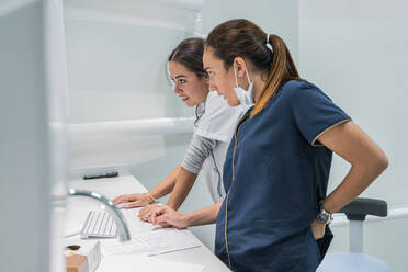 Seitenansicht eines Mediziners, der im Labor eines modernen Krankenhauses gemeinsam Daten auf einem modernen Computer durchsucht - ADSF37791