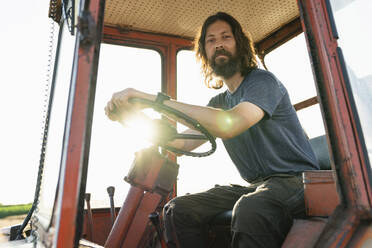 Smiling mature farmer sitting in tractor on sunny day - EKGF00006