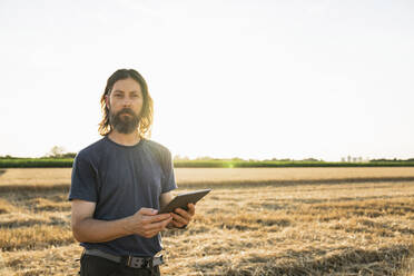 Bärtiger Bauer mit Tablet-PC auf einem Bauernhof an einem sonnigen Tag - EKGF00012
