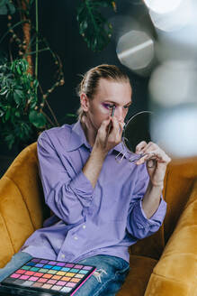 Man applying eyeshadow sitting on chair - YTF00011