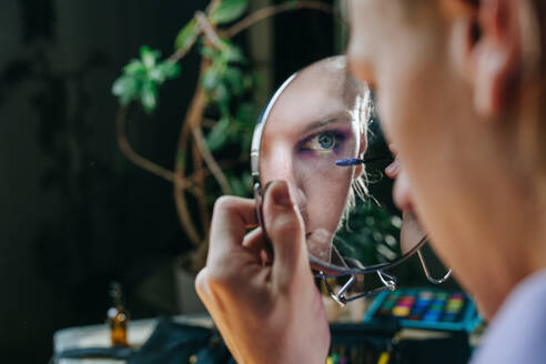 Reflection of man applying mascara in hand mirror - YTF00013