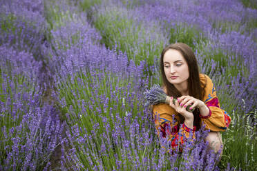 Nachdenkliche Frau mit Lavendelblumenstrauß auf einem Feld - YLF00005