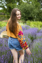 Happy woman with basket touching lavender flower plants at field - YLF00008