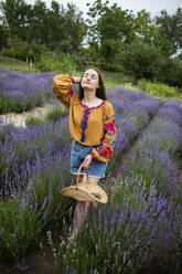 Woman with eyes closed standing amidst lavender plants at field - YLF00011