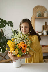 Smiling girl hugging flower vase at table in kitchen - LESF00134
