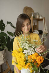 Smiling girl touching flowers in vase at home - LESF00135