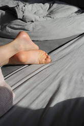Mädchen auf dem Bett liegend mit gekreuzten Beinen - GISF00902