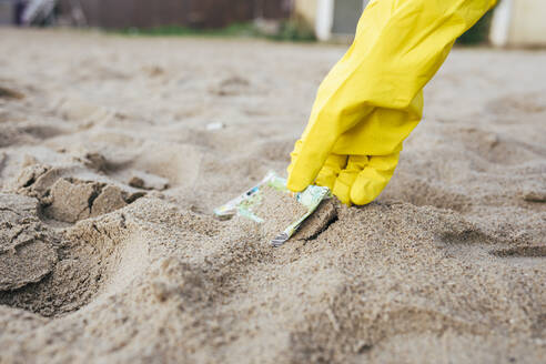 Hand einer Frau, die am Strand Abfälle aus dem Sand aufnimmt - OYF00734