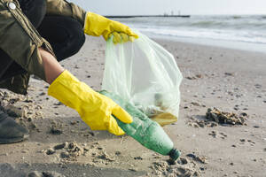 Hände von Umweltschützern, die am Strand Plastikflaschen in Müllsäcken sammeln - OYF00741