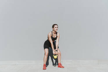 Young woman with kettlebell exercising in front of gray wall - OIPF02348
