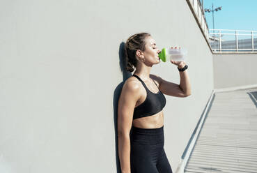 Woman drinking water from bottle leaning on wall - OIPF02365