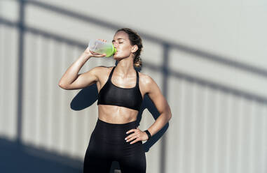 Young athlete with hand on hip drinking water in front of wall - OIPF02376