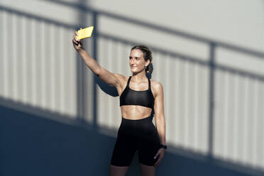 Lächelnder junger Sportler, der ein Selfie mit seinem Mobiltelefon macht - OIPF02381