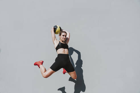 Sportler mit Medizinball, der vor eine graue Wand springt - OIPF02412