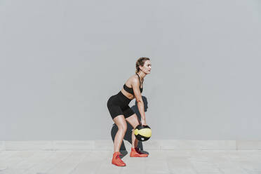 Woman with medicine ball exercising in front of gray wall on sunny day - OIPF02414