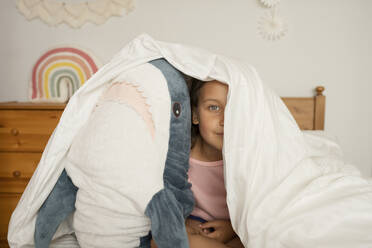 Mädchen versteckt sich unter einer Decke mit Hai-Spielzeug im Kinderzimmer - LESF00149