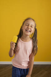 Glückliches Mädchen mit Eis vor einer gelben Wand - LESF00158