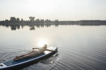 Frau paddelt mit Hand auf dem Paddelbrett liegend bei Sonnenuntergang - EYAF02162