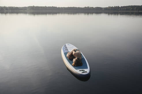 Frau in Embryo-Pose auf Paddleboard am See liegend - EYAF02165