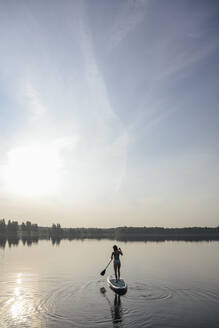 Woman doing standup paddleboarding in lake - EYAF02167