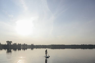 Frau macht Standup-Paddleboarding in See unter Himmel - EYAF02168