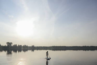 Woman doing standup paddleboarding in lake under sky - EYAF02168