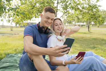 Junger Mann und Frau unterhalten sich per Videoanruf über ein Smartphone im Park - LESF00163