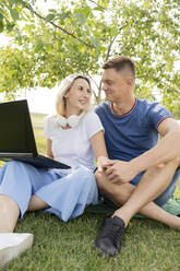 Junge Frau sitzt mit Laptop und hält die Hand ihres Freundes im Park - LESF00168