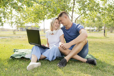 Affectionate young woman and man with laptop spending leisure time in park - LESF00169