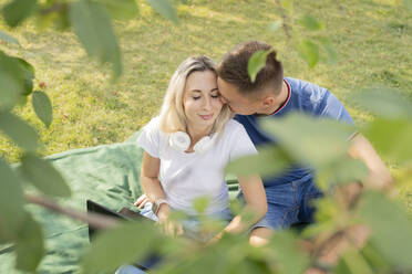 Affectionate young man kissing girlfriend enjoying picnic at park - LESF00170