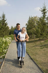 Junge Frau und ihr Freund genießen eine Fahrt mit dem Elektroroller im Park - LESF00173