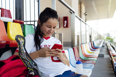 Lächelnder Spieler, der im Stadion mit seinem Smartphone SMS schreibt - PGF01305