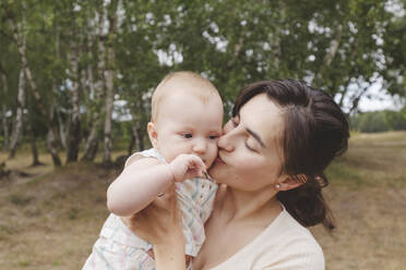 Mother kissing her daughter in park - IHF01216