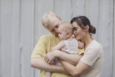 Mutter und Vater umarmen ihre Tochter vor einer Mauer - IHF01223