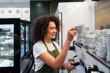 Side view barista with portafilter and cup preparing aromatic drink in coffee machine in cafe - ADSF37849