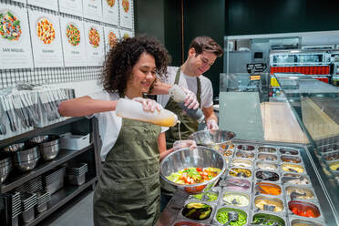 Lächelnde Verkäuferinnen und Verkäufer in Schürzen bereiten Salate in einer Bar in einem modernen Supermarkt zu - ADSF37862