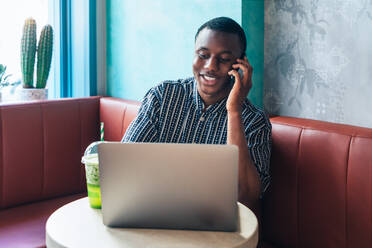 Inhalt Afroamerikanischer männlicher Unternehmer, der in einem Restaurant mit Netbook und Smoothie am Tisch telefoniert - ADSF37865