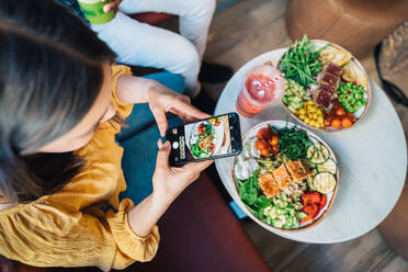 Oben: anonymer weiblicher Vlogger mit schwarzem Partner, der mit seinem Handy im Restaurant ein Foto von einer gesunden Mahlzeit macht - ADSF37870