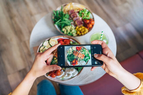 From above of crop unrecognizable female vlogger taking photo of delicious power bowl on cellphone in restaurant - ADSF37875