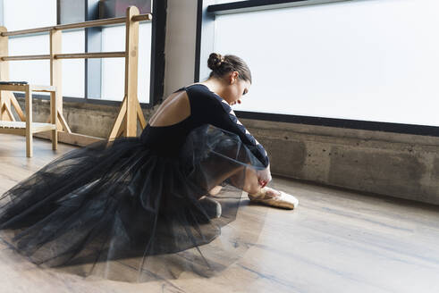 Junge Tänzerin sitzt auf dem Boden eines Tanzstudios und zieht Ballettschuhe an - ADSF37898