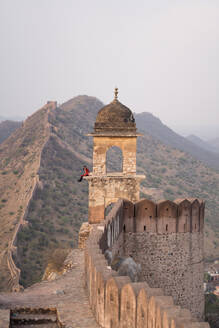 Frau sitzt im Gewölbe des alten Turms vor dem Bergkamm und den Mauern beim Besuch des Aussichtspunkts Amer Fort in Jaipur, Indien - ADSF37909