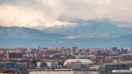 Scenic view of city of Madrid with residential buildings on background of snowy mountains on sunny day - ADSF37917