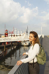 Smiling woman standing by railing on sunny day - IHF01227