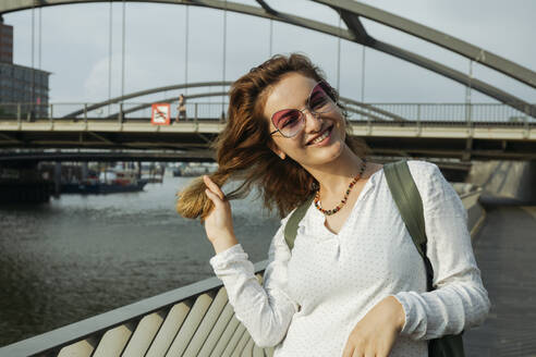 Glückliche Frau mit Brille vor einer Brücke, Hamburg, Deutschland - IHF01235