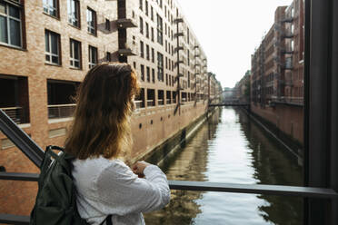Woman standing by railing in front of buildings at Speicherstadt, Hamburg, Germany - IHF01238