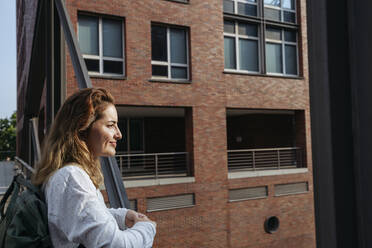 Smiling woman standing by railing in front of building - IHF01239